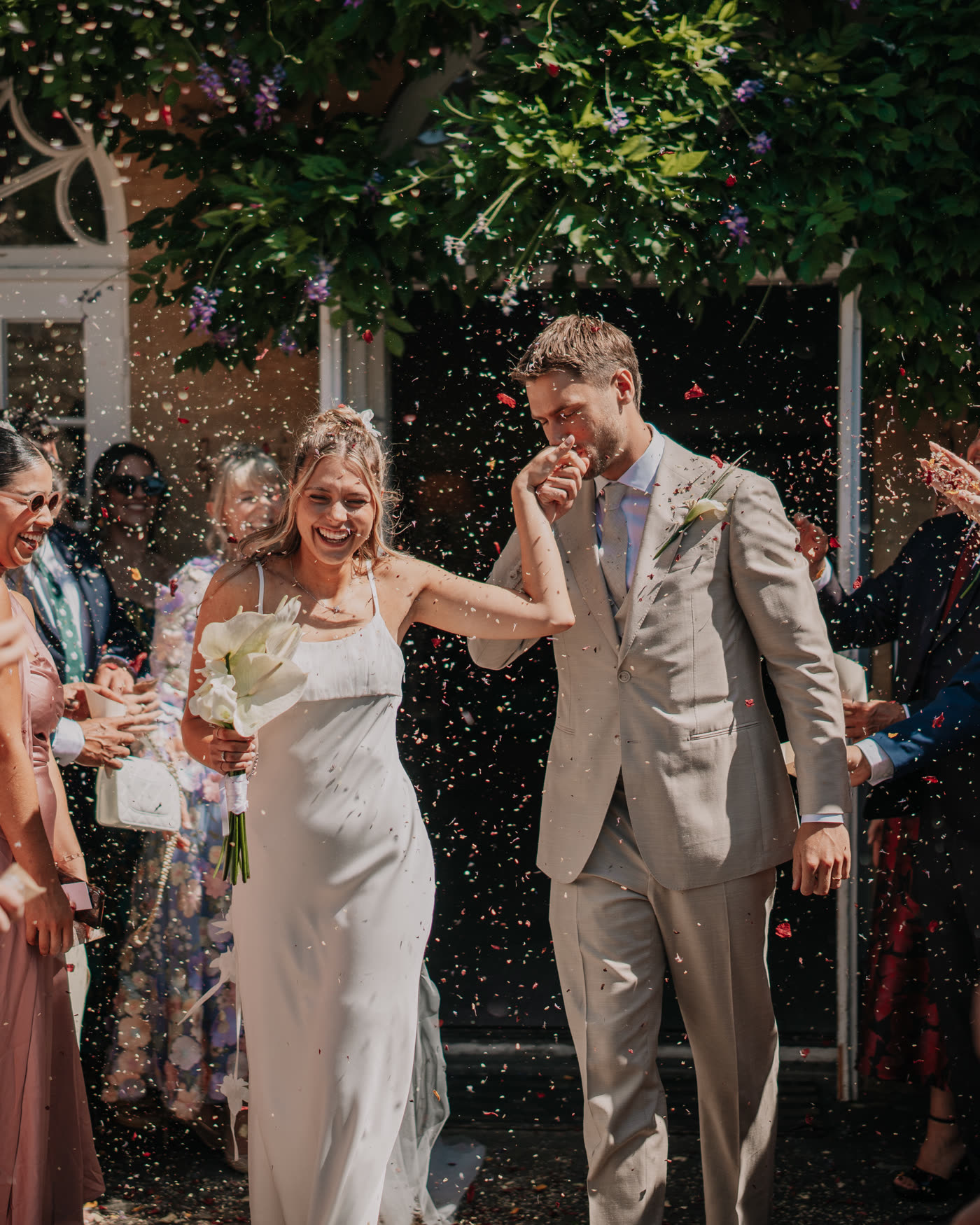 A couple walking out through a confetti throw, guests either side